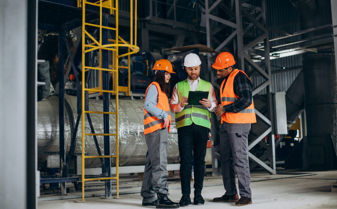 Three factory workers in safety hats discussing manufacture plan