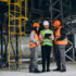 Three factory workers in safety hats discussing manufacture plan